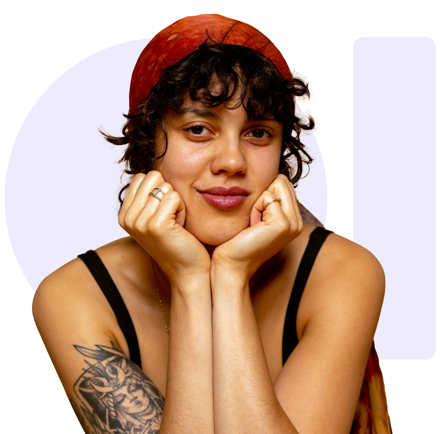 A smiling woman with curly hair and a red headscarf rests her chin on her hands