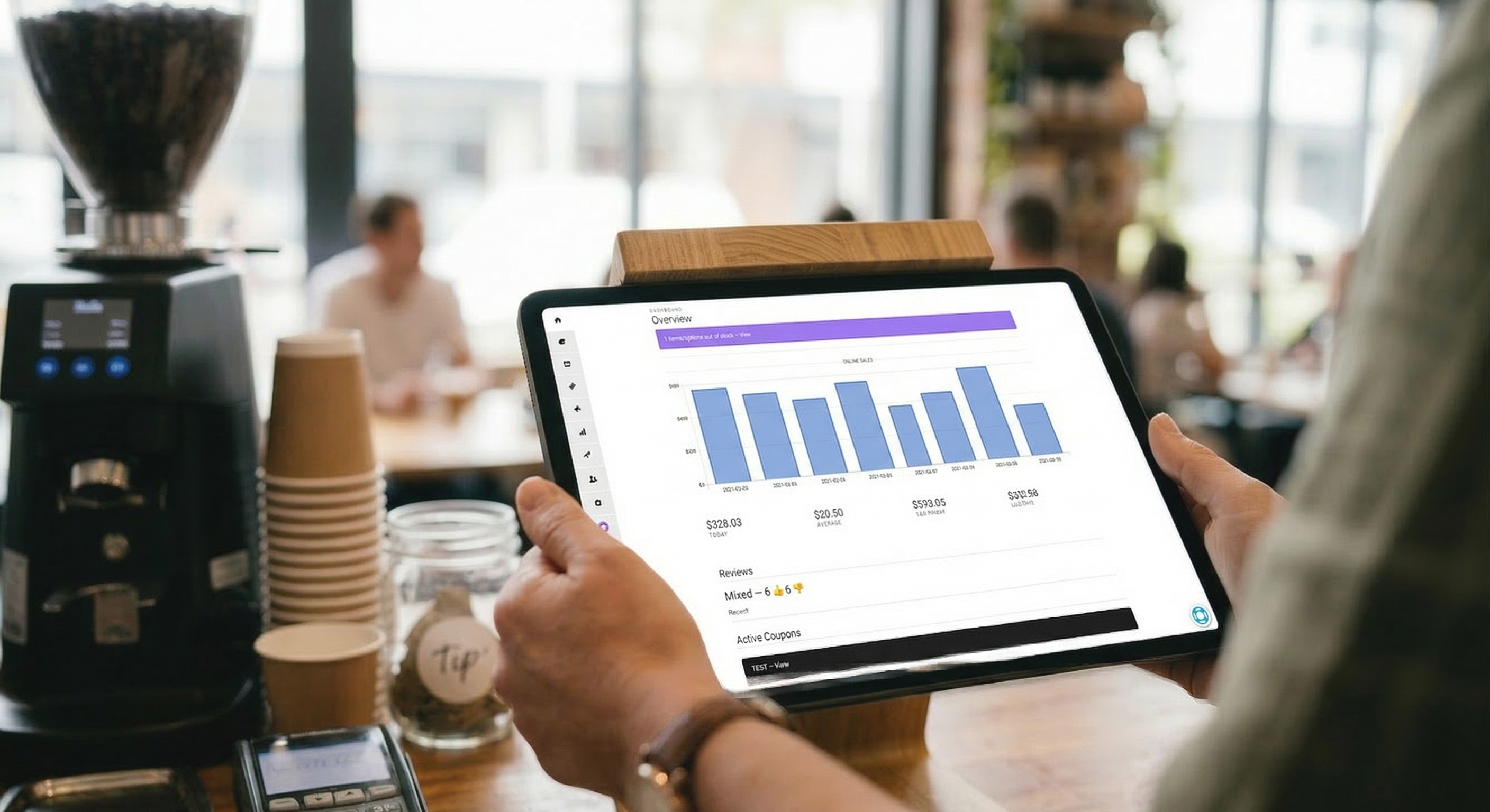 Restaurant owner checking order performance reports on a tablet in a cafe environment.