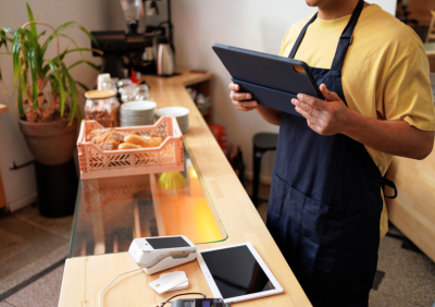 A cafe staff member in an apron reviewing information on a tablet at the counter.