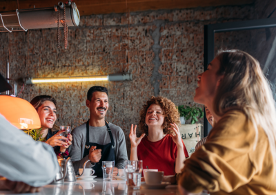 A group of friends at a restaurant table, laughing and enjoying a meal while a staff member attends to them.