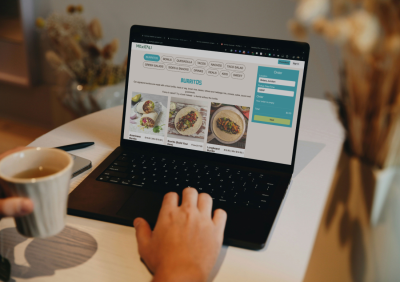 A person browsing a food ordering website on a laptop, with menu items visible on screen.