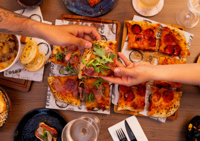 Friends sharing flatbread pizzas at a restaurant table, hands reaching in to take slices.