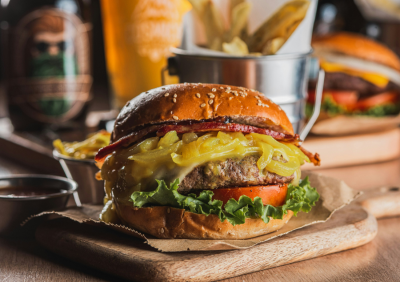 A loaded cheeseburger on parchment paper with fries and drinks in the background.